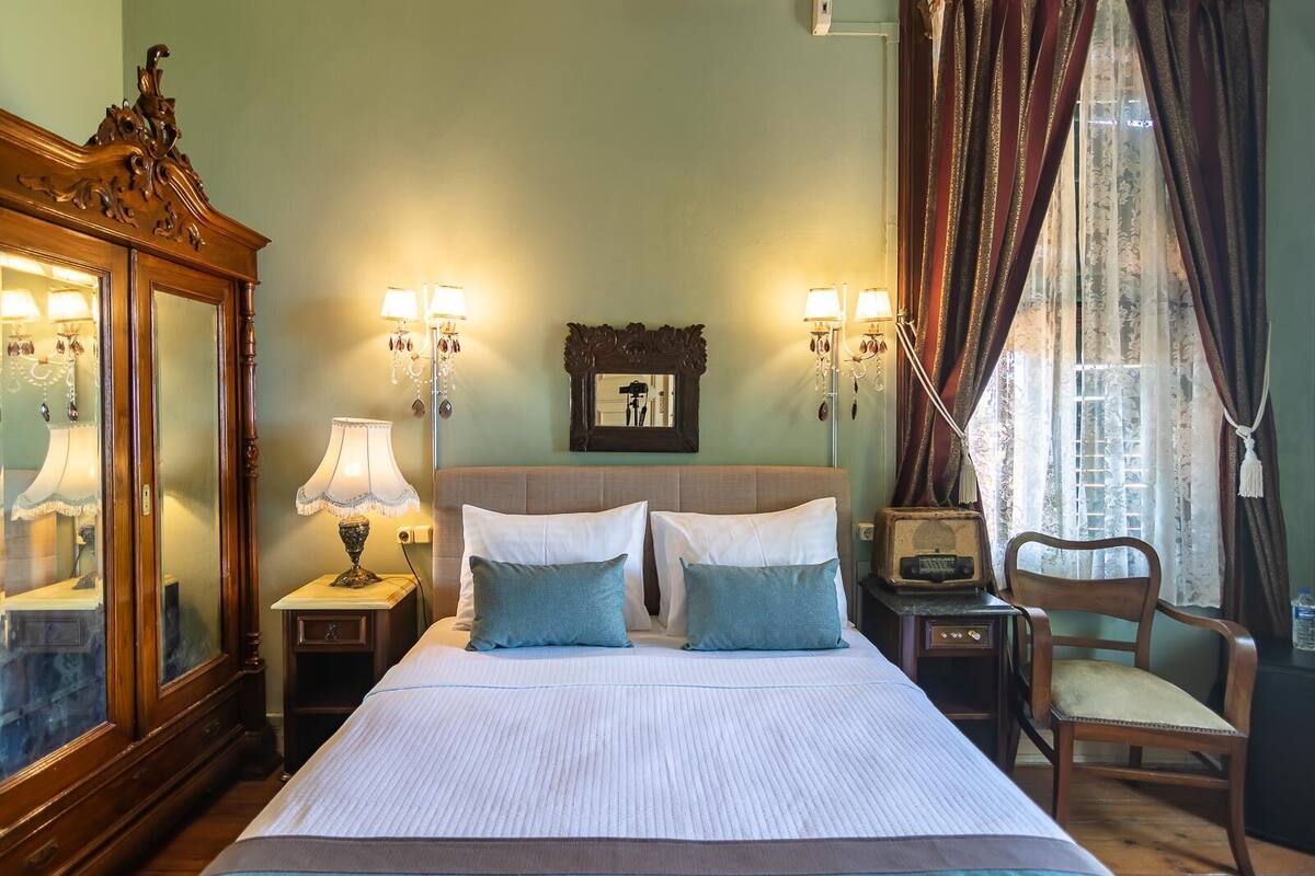 Une chambre d’hôtel avec un grand lit, deux lampes de chevet, un miroir, une commode et une chaise.