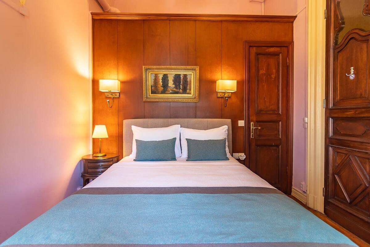 Une chambre d’hôtel avec un grand lit, deux lampes de chevet, un tableau encadré au mur et une porte en bois.