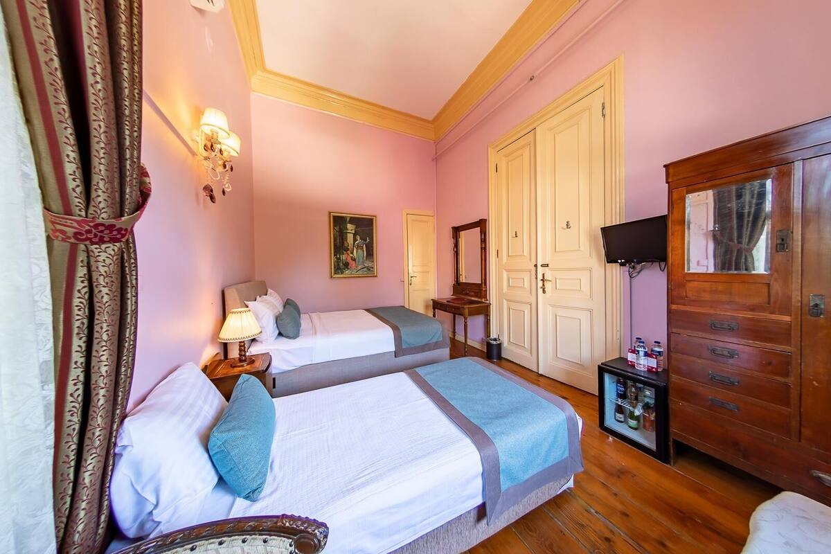 Une chambre avec deux lits, une armoire en bois, une télévision et un tableau au mur.