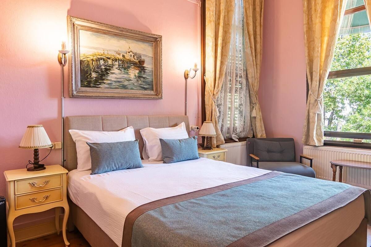 Un lit bien fait, avec des oreillers, une lampe de chevet, une chaise et un tableau accroché au mur.