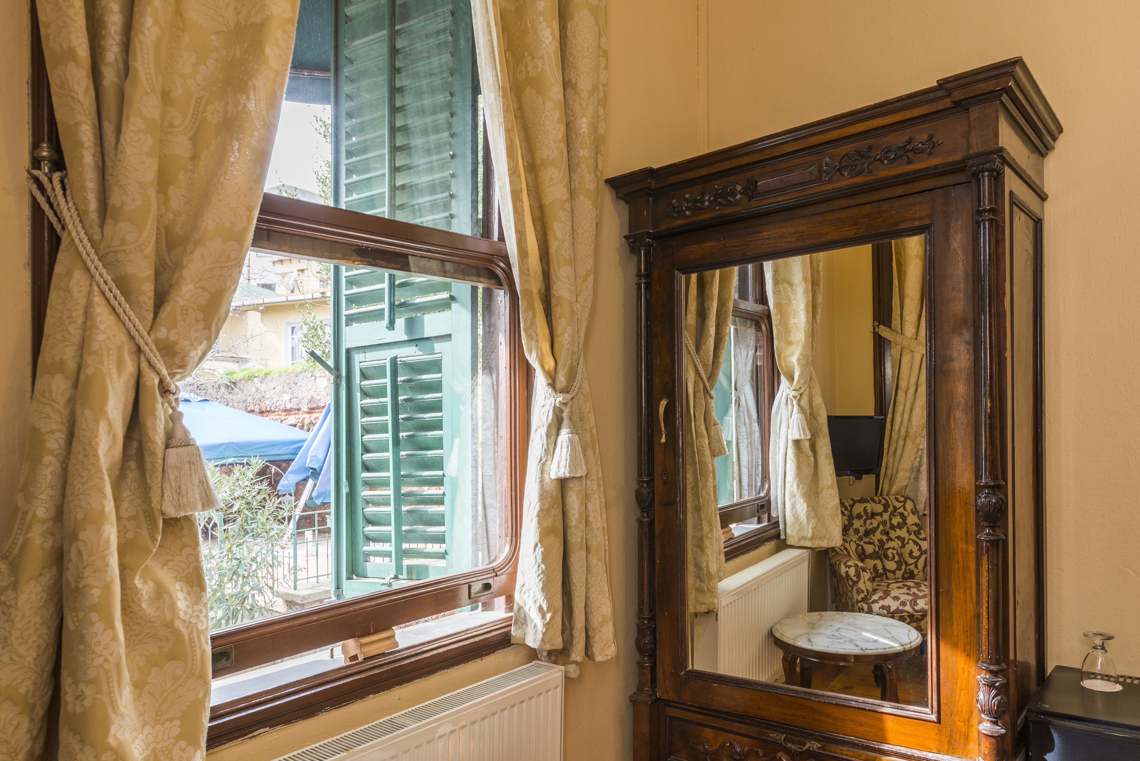 A room with a large mirror, a window with green shutters, and a radiator.