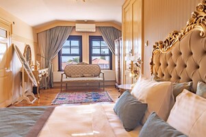 Un dormitorio lujoso con una cama grande, un sillón, un espejo decorativo y vistas al exterior a través de amplias ventanas.