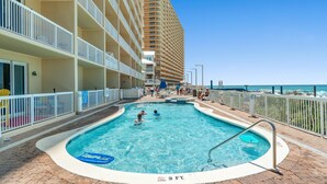 Ein Poolbereich eines Hotels mit einem klaren blauen Pool, einem Rettungsschwimmerstand und einer Wassertiefe von 3 Fuß.