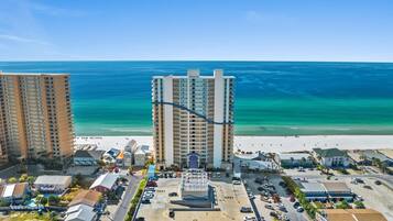 A coastal hotel with multiple high-rise buildings, a parking lot, and a beach in the background.