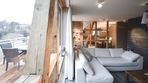 A modern living room with a white sofa, wooden beams, and a view of the city. - Stadt Chalet (Braunlage)