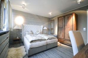 A bedroom with a large bed, two bedside tables with lamps, a wooden wardrobe, and a chair.