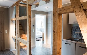 A modern interior with exposed wooden beams, a kitchen with a marble backsplash, and a staircase leading to a bedroom.