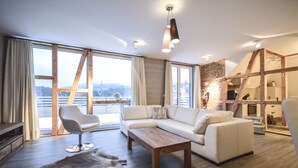 A modern living room with a white sofa, a wooden coffee table, and a fur rug. There is a large window with curtains, a wooden ladder, and a bookshelf. - Stadt Chalet (Braunlage)