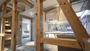 A modern interior with exposed wooden beams, a kitchen area with a marble backsplash, and a view of a snowy landscape through a window. - Stadt Chalet (Braunlage)