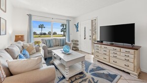 Sala de estar con sofá, mesa de centro, televisor y vistas al exterior.