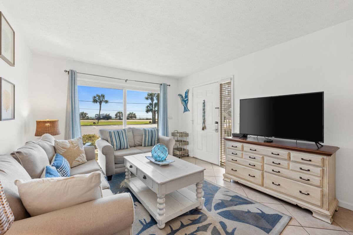 A living room with a sofa, coffee table, TV, and a view of the outdoors.