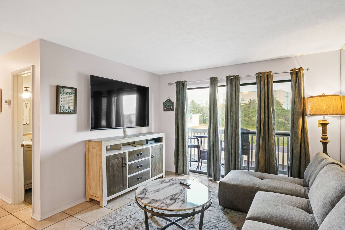 A living room with a TV, sofa, and a balcony with curtains.