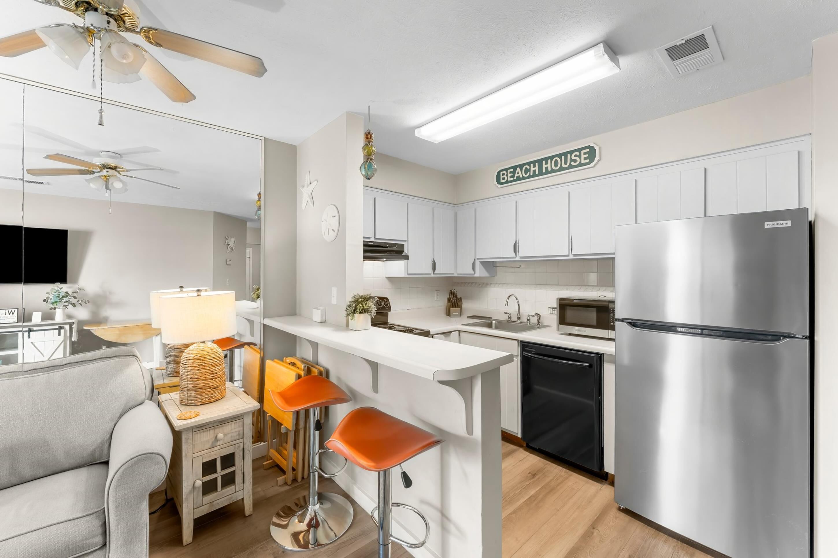 A modern kitchen with white cabinets, a stainless steel refrigerator, and a bar area with stools.