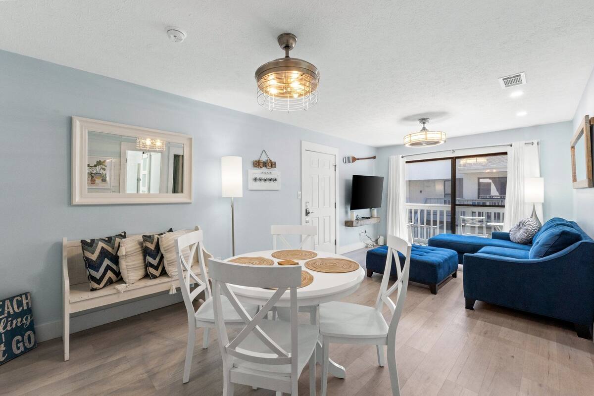 A modern living room with a round dining table, white chairs, a blue sofa, and a television.