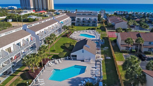 Un resort con varias piscinas, un edificio grande con balcones y vista al océano.