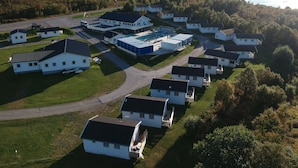 An aerial view of a residential area with white houses, a large blue building, and a bridge in the background. - Tjeldsundbrua Camping (Tjeldsund)
