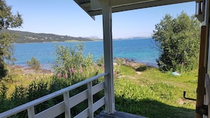 A wooden deck with a white railing overlooking a body of water, surrounded by greenery and trees. - Tjeldsundbrua Camping (Tjeldsund)