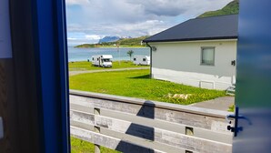 A view of a white building with a dark roof, a grassy area, and a body of water in the background. - Tjeldsundbrua Camping (Tjeldsund)