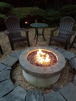 Un focolare in pietra circolare con due poltrone Adirondack e un tavolino con una candela.