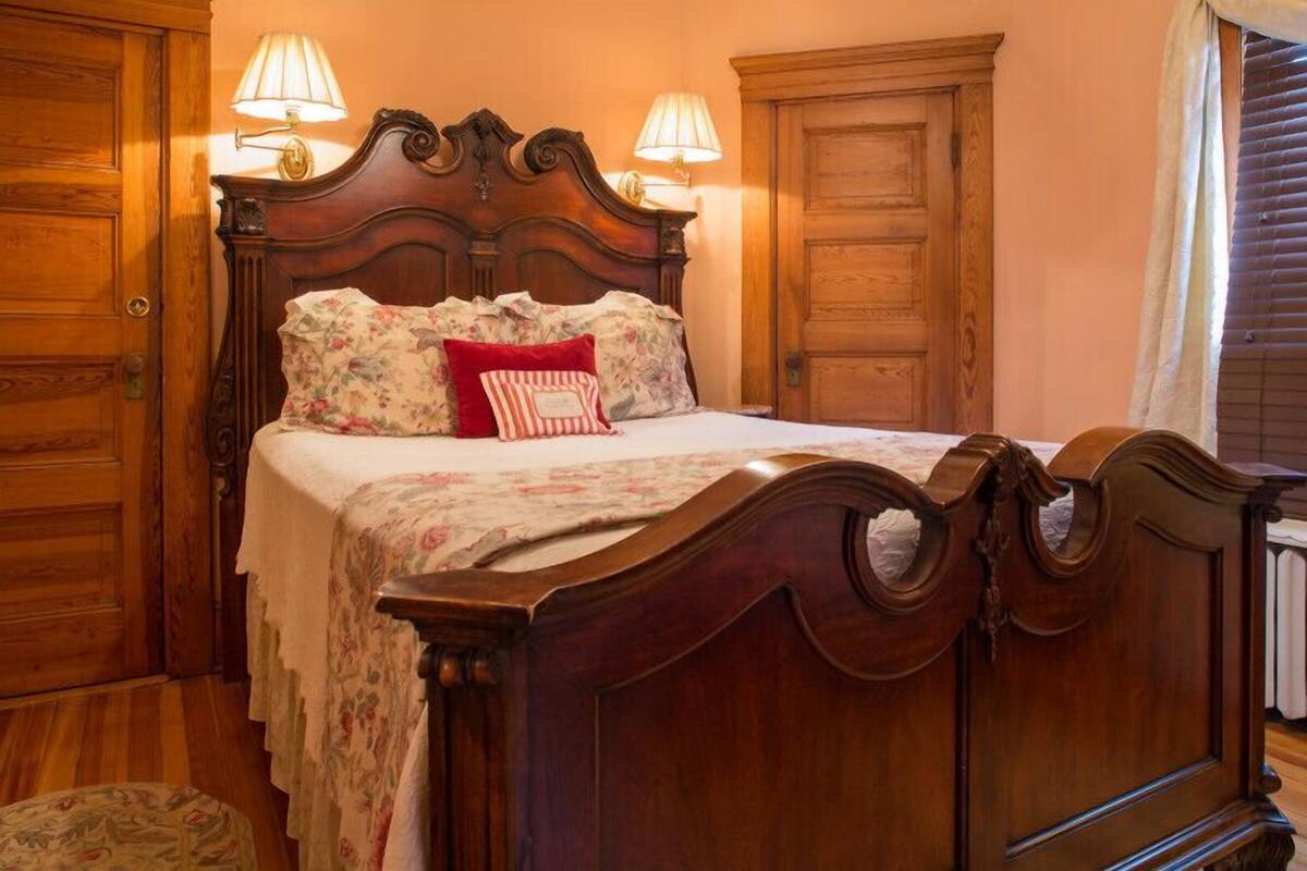 Una cama con dosel de madera con ropa de cama floral y dos lámparas a cada lado.
