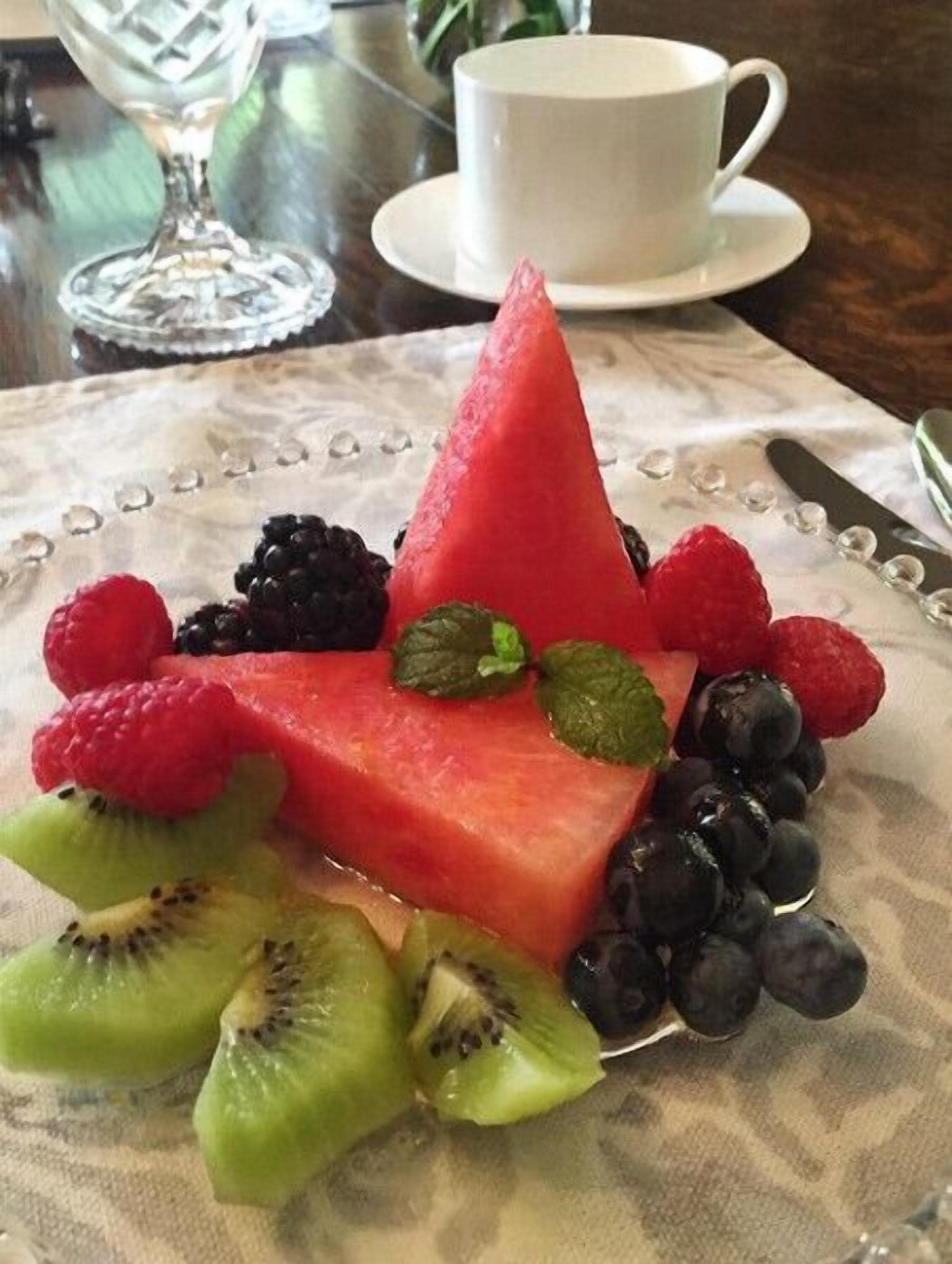 A plate of watermelon and assorted berries with a cup and glass in the background.