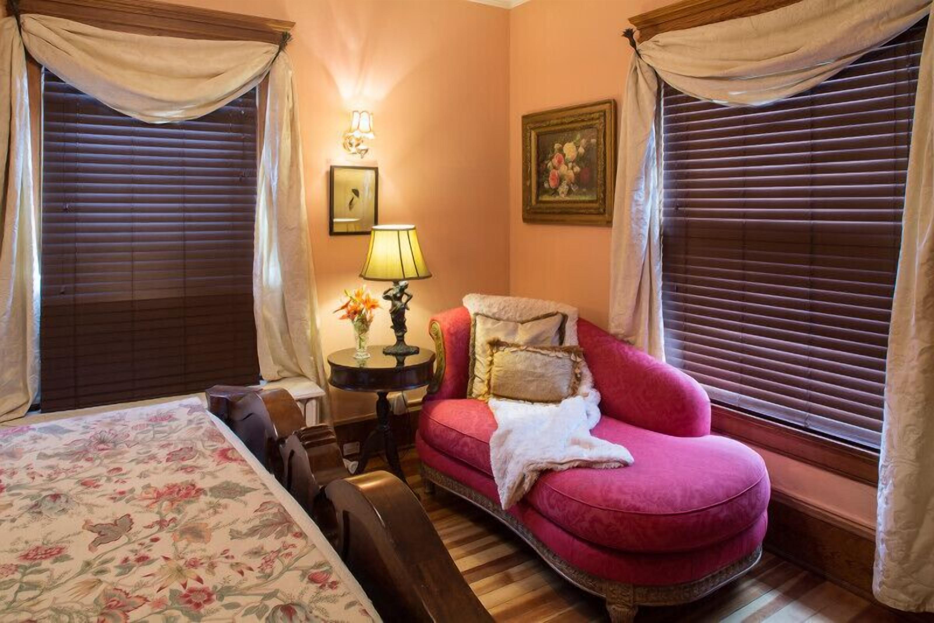 Un dormitorio con una cama, un sillón rojo, una mesita de noche con lámpara y un cuadro en la pared.