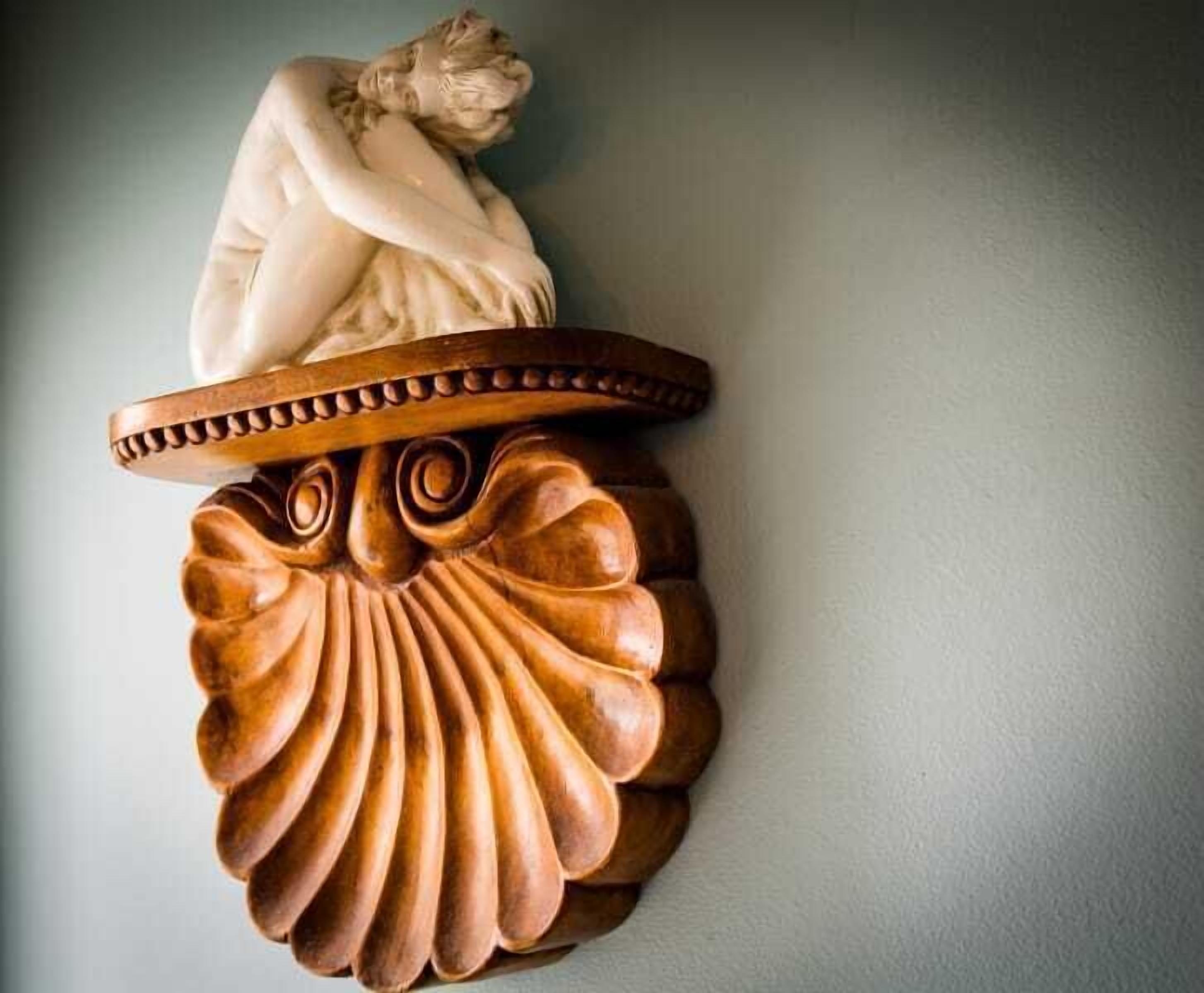 Une sculpture en bois représentant une figure posée sur un socle incurvé.