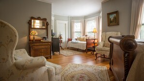 Una habitación tradicional con un aparador de madera, una cama con dosel blanco, una silla y una mesa con lámpara.