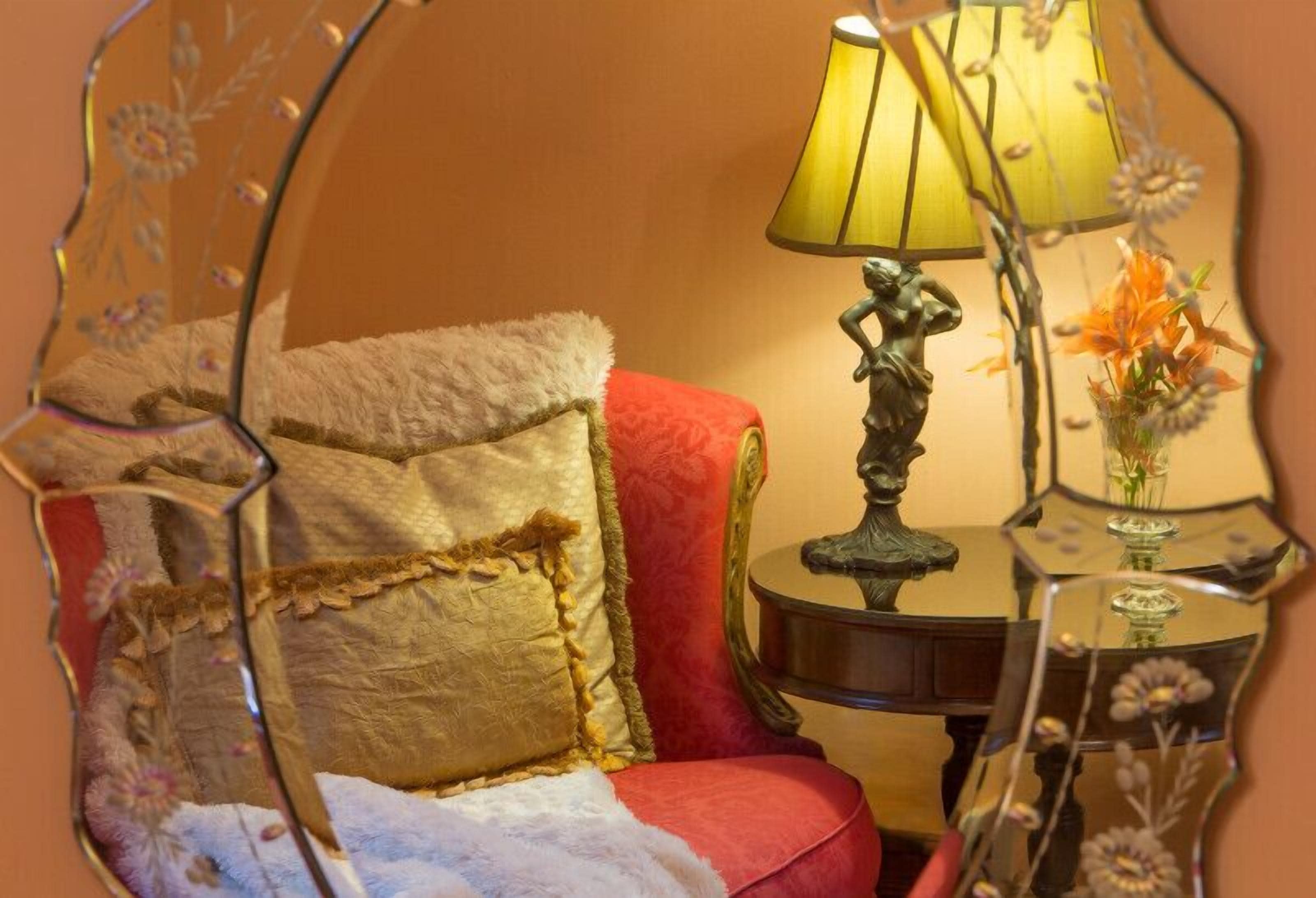 A cozy room with a red armchair, a small table with a lamp, and a mirror reflecting the room's decor.
