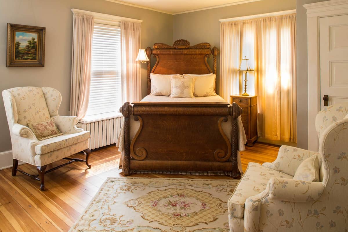 Un dormitorio con una cama grande, dos sillones, una mesita de noche y una ventana con cortinas.