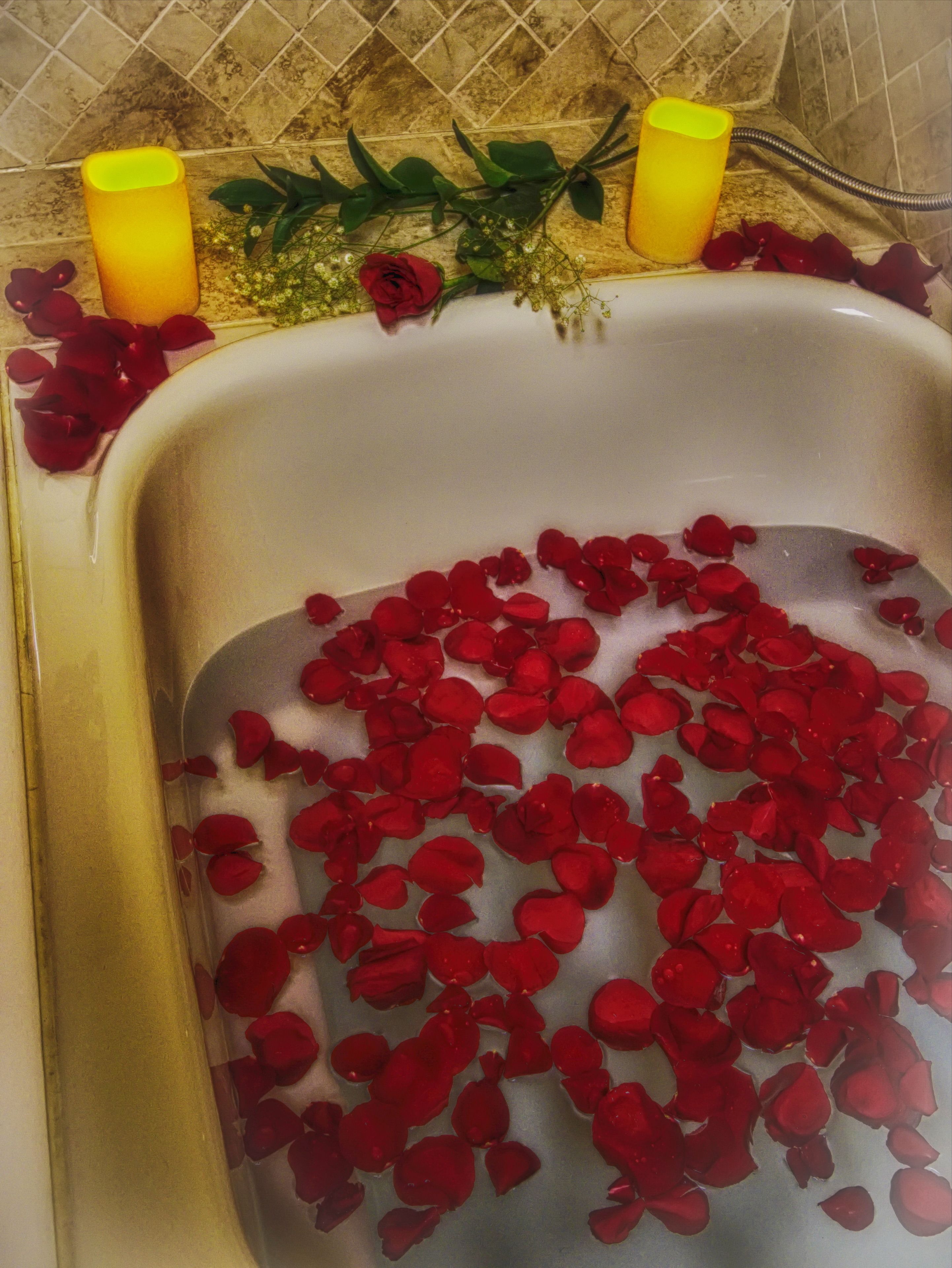 A bathtub filled with rose petals and surrounded by candles and greenery.