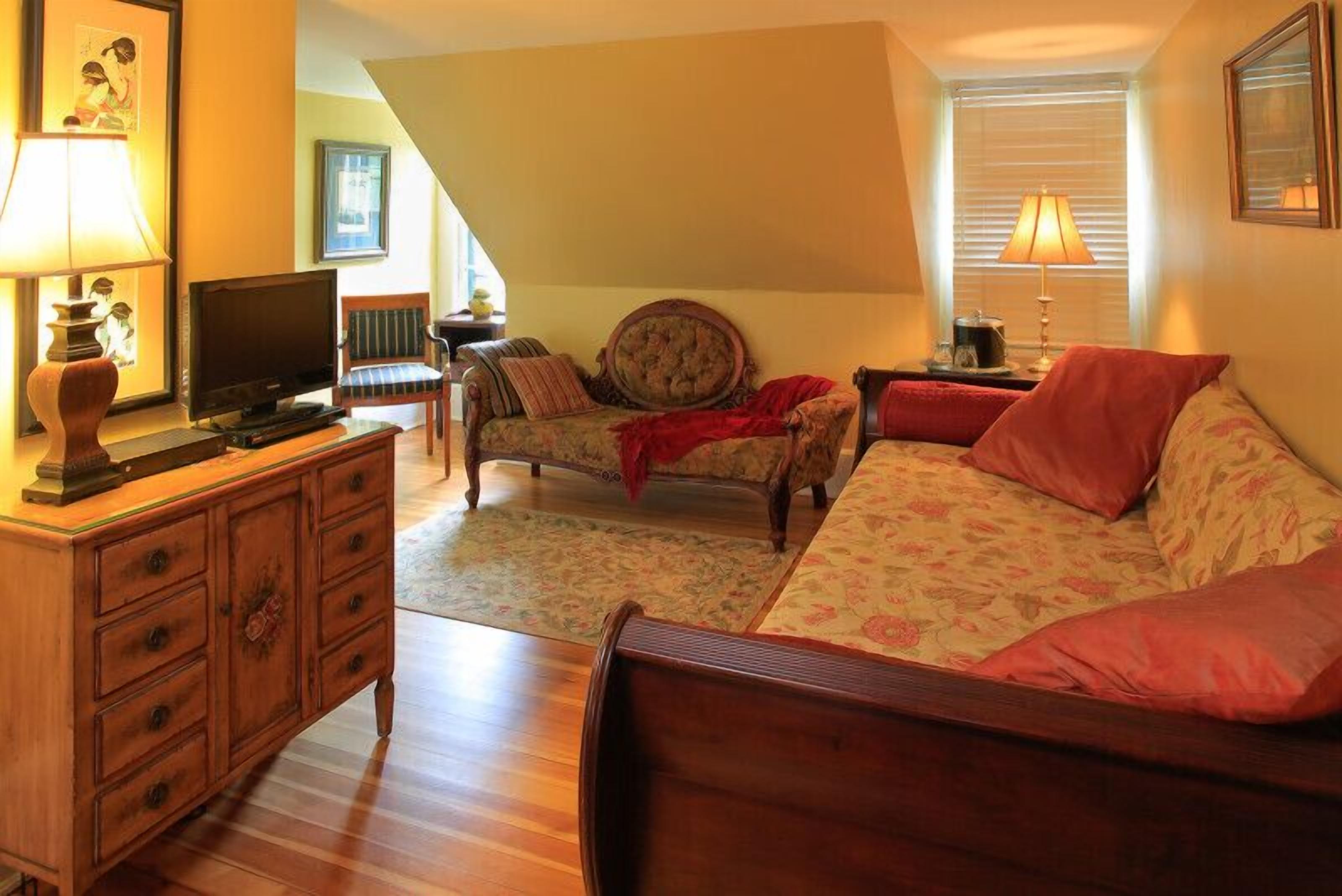 A cozy room with a wooden bed, a sofa, a chair, a TV, and a dresser.