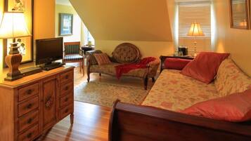 A cozy room with a wooden bed, a sofa, a chair, a TV, and a dresser.