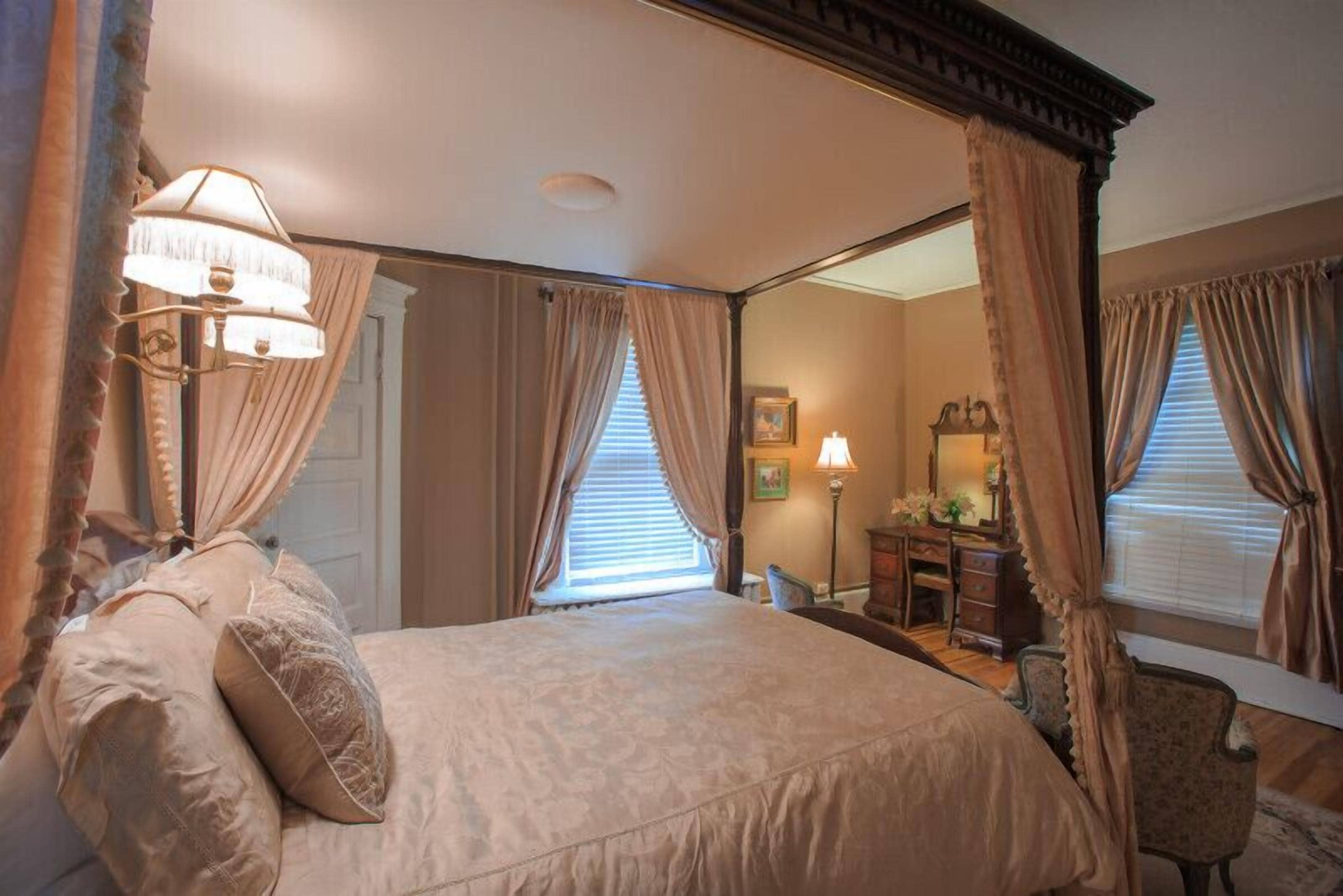 A bedroom with a four-poster bed, a mirror, and curtains.