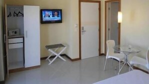 A hotel room with a television, a small table, a chair, and a wardrobe. - Barra Mar Hotel (Salvador)