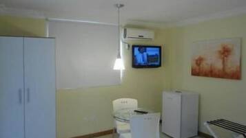 Una habitación pequeña y con pocos muebles, con una cama individual, un escritorio, una silla, un televisor y un radiador.