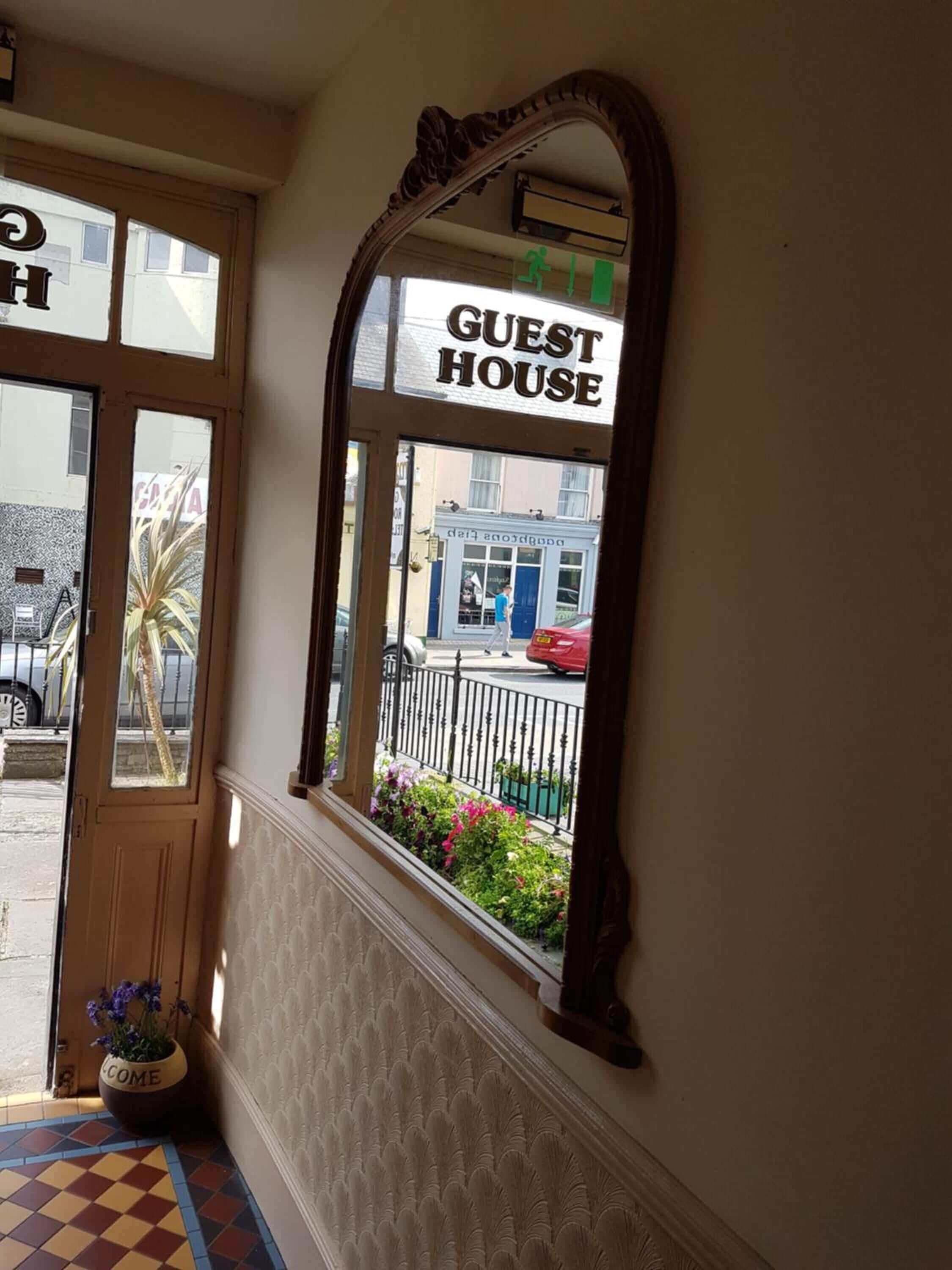 Una puerta con un letrero que dice 'GUEST HOUSE', un espejo y vista de la calle.