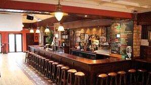 A bar area with a long counter, stools, and a menu board. - Myles Creek Guesthouse (Kilkee)