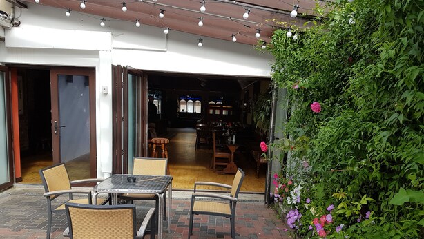 An outdoor patio with a brick floor, wicker chairs, and a table. - Myles Creek Guesthouse (Kilkee)