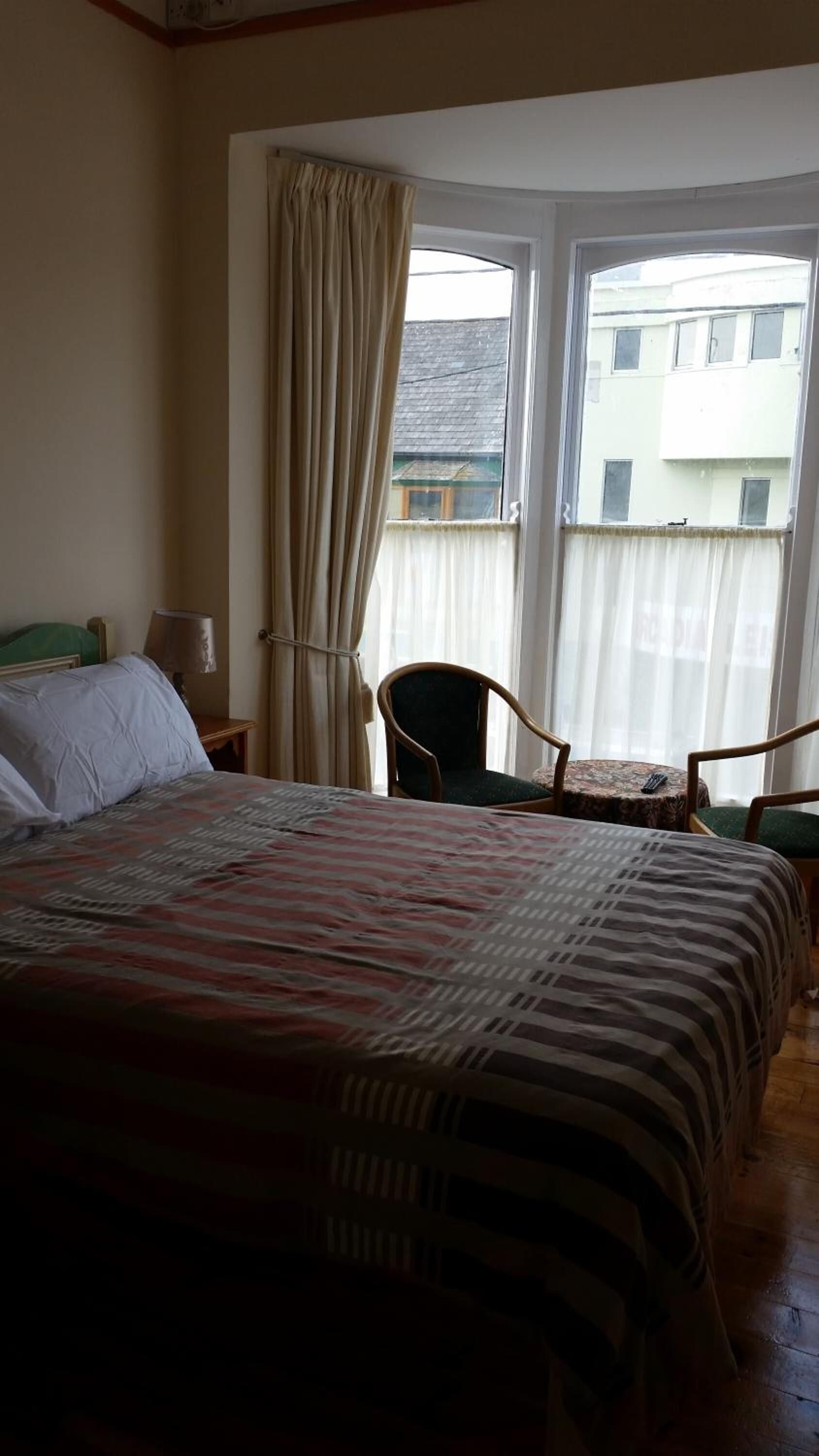 A hotel room with a large bed, a chair, a small table, and a window with curtains.