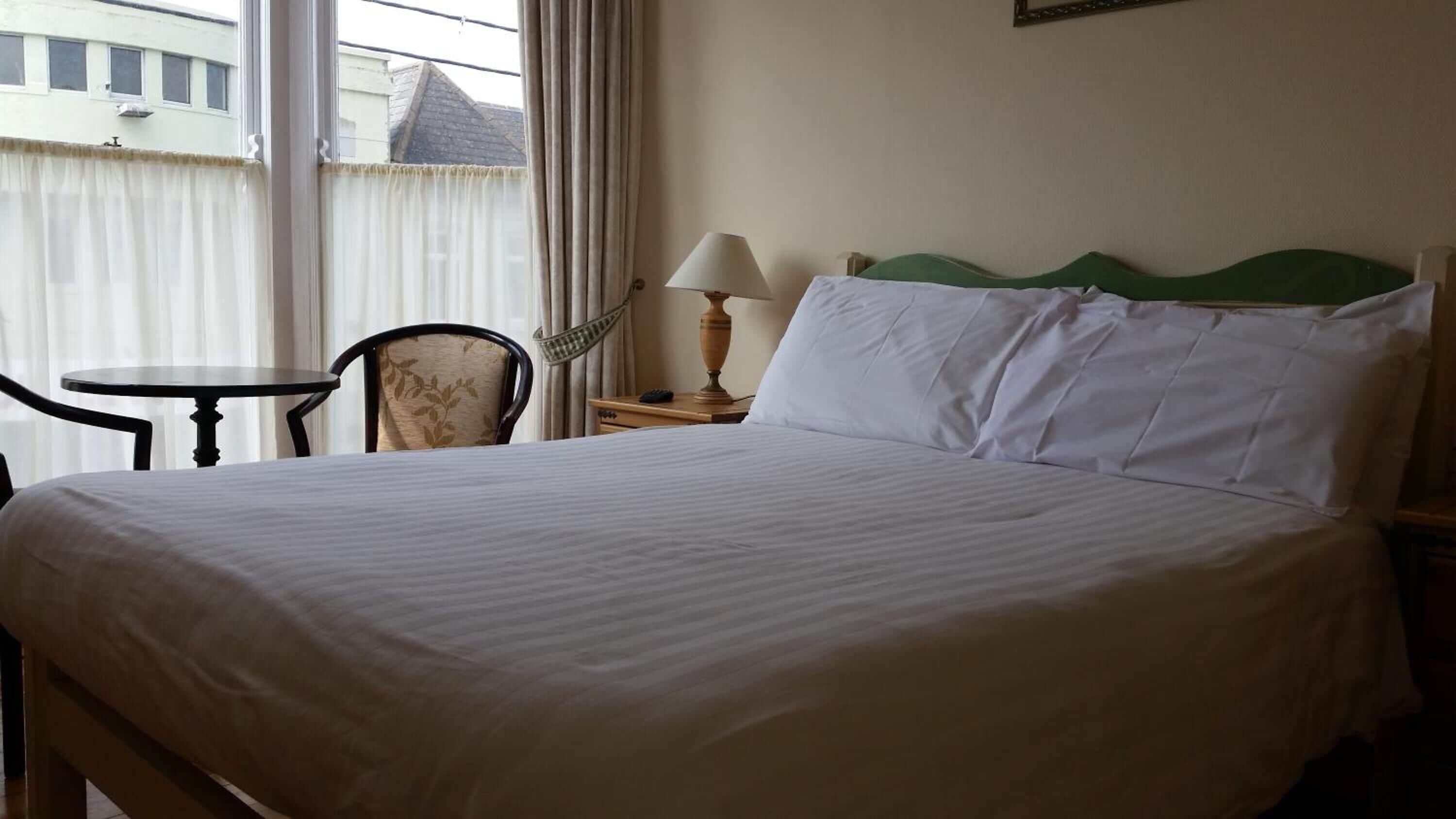 Una habitación de hotel con una cama grande, una mesita pequeña, una silla y una lámpara.