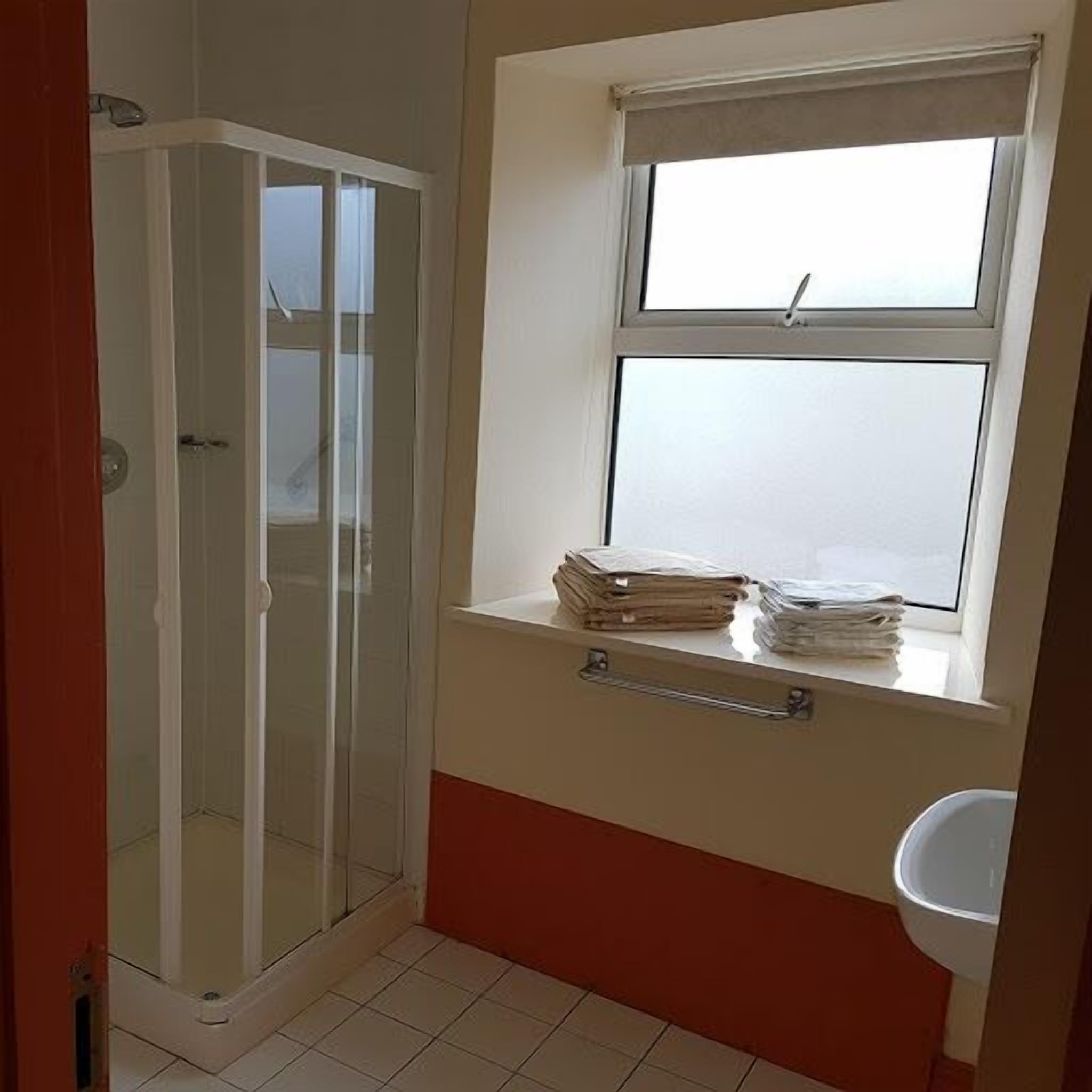 A bathroom with a shower, a window with a view, and a sink.