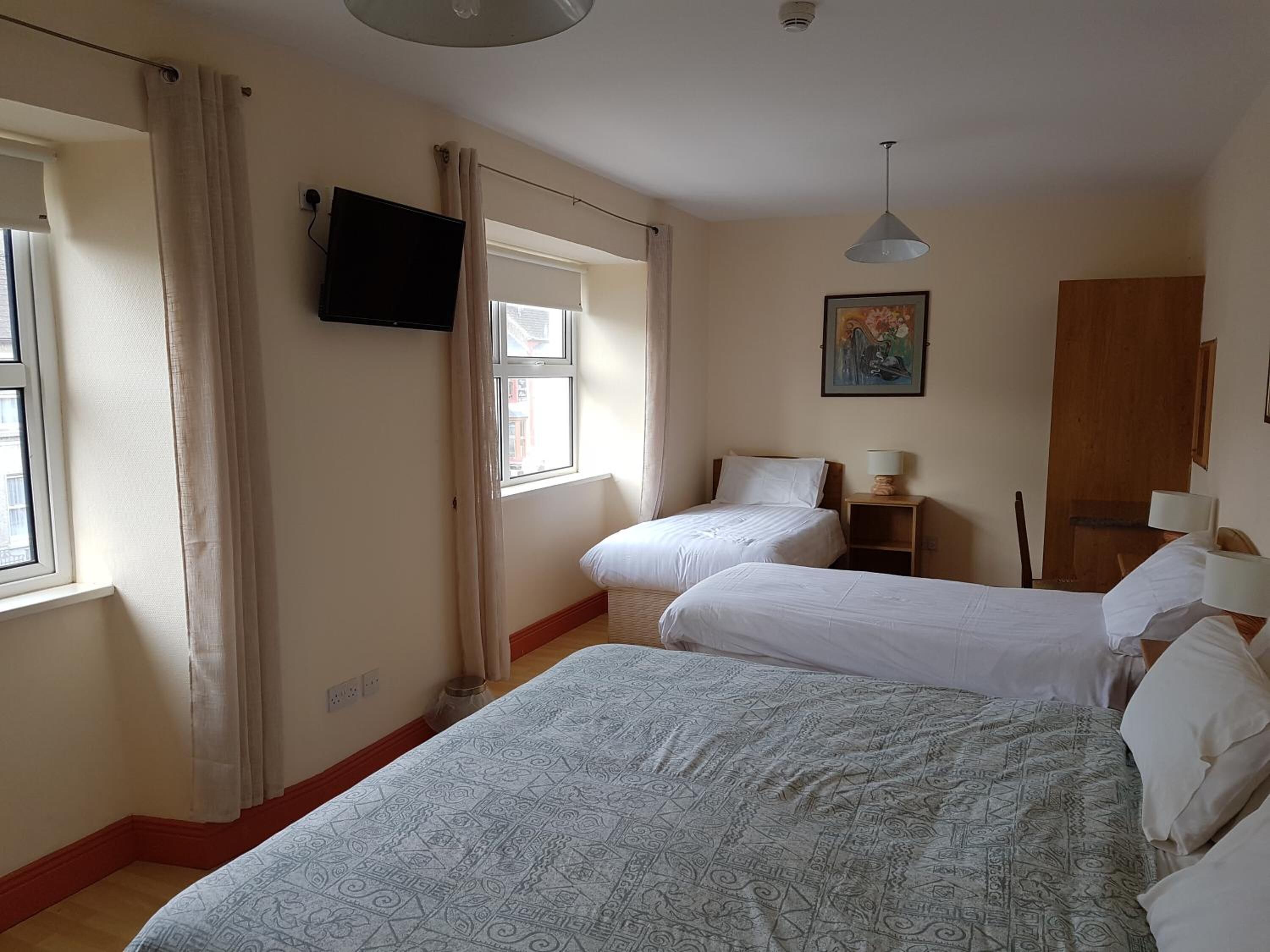 A hotel room with two beds, a television, a painting, and a window with curtains.
