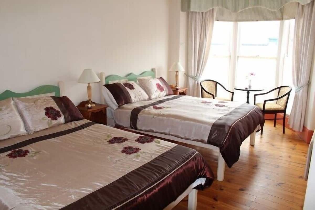 Quarto de hotel com duas camas, uma mesinha, cadeiras e uma janela com cortinas.