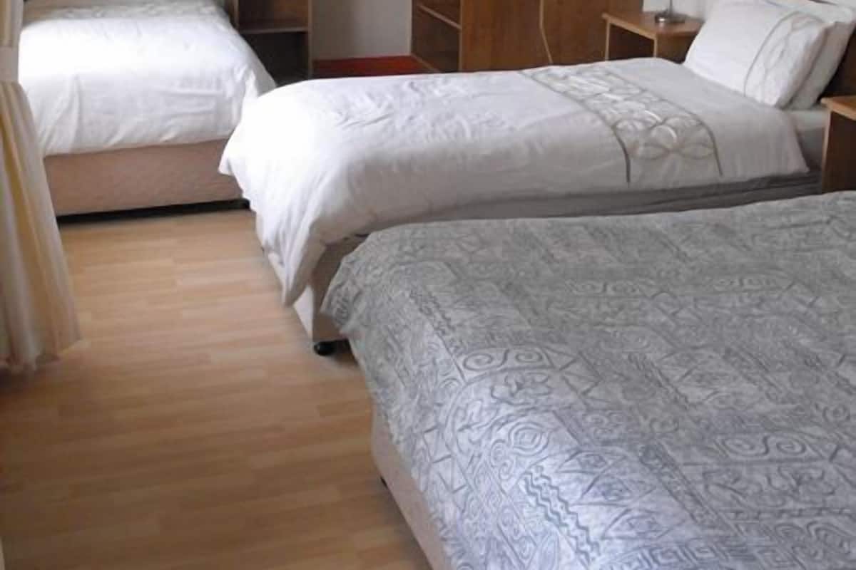 Quarto de hotel com duas camas de solteiro, um guarda-roupa de madeira, uma escrivaninha e um candeeiro suspenso.