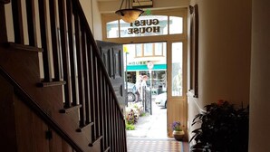 A hallway with a wooden staircase, a tiled floor, and a view of a storefront with a 'HOUSE' sign. - Myles Creek Guesthouse (Kilkee)