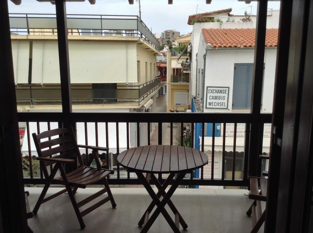 A balcony with a table and chairs, overlooking a street with buildings and a sign that reads 'EXCHANGE CAMBIO WECHSEL'.