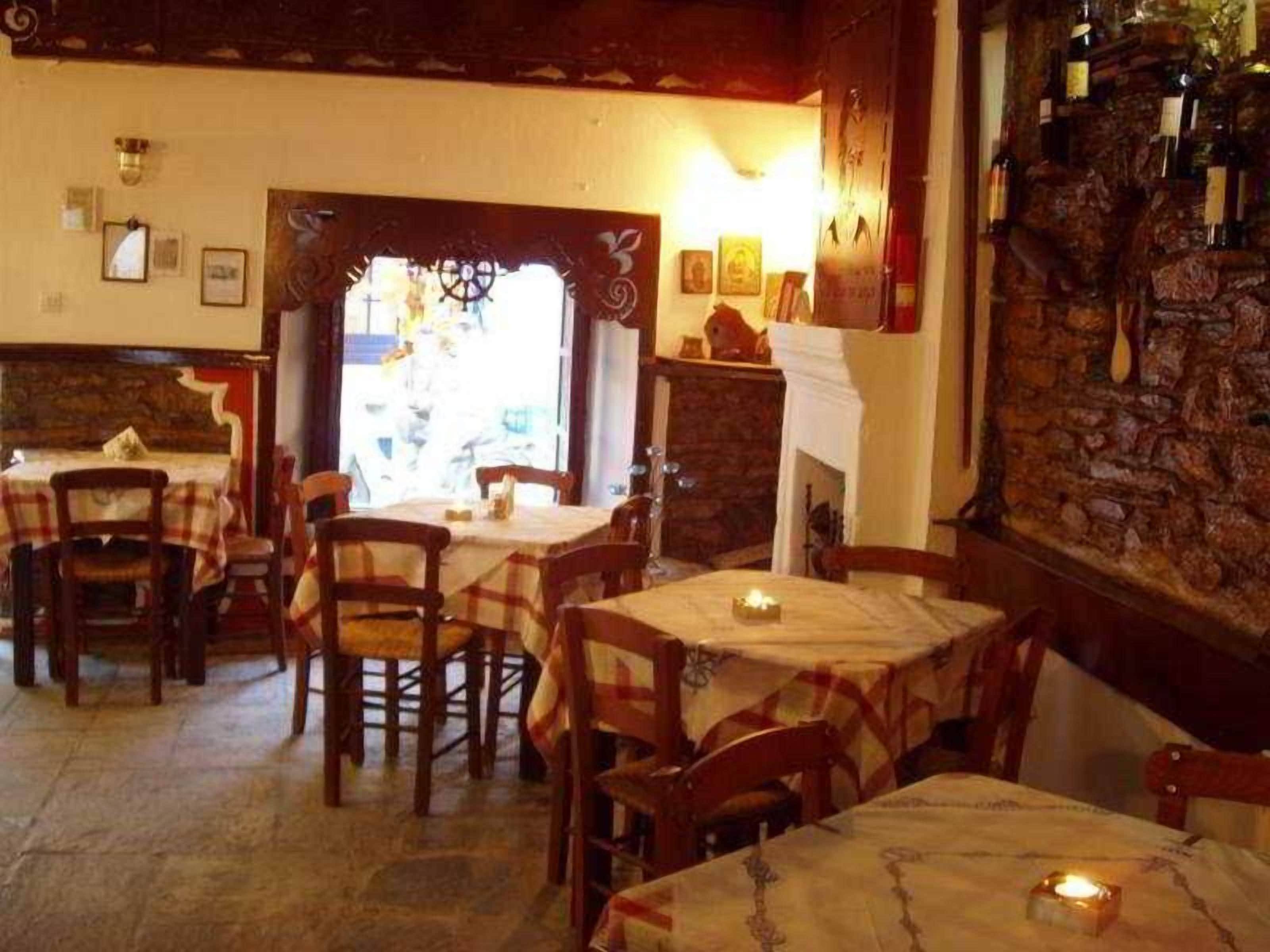 Een restaurantinterieur met meerdere tafels en stoelen, een stenen muur met flessen en een open haard.