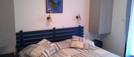 A bed with striped bedding, two wall-mounted lamps, and a painting above the bed.