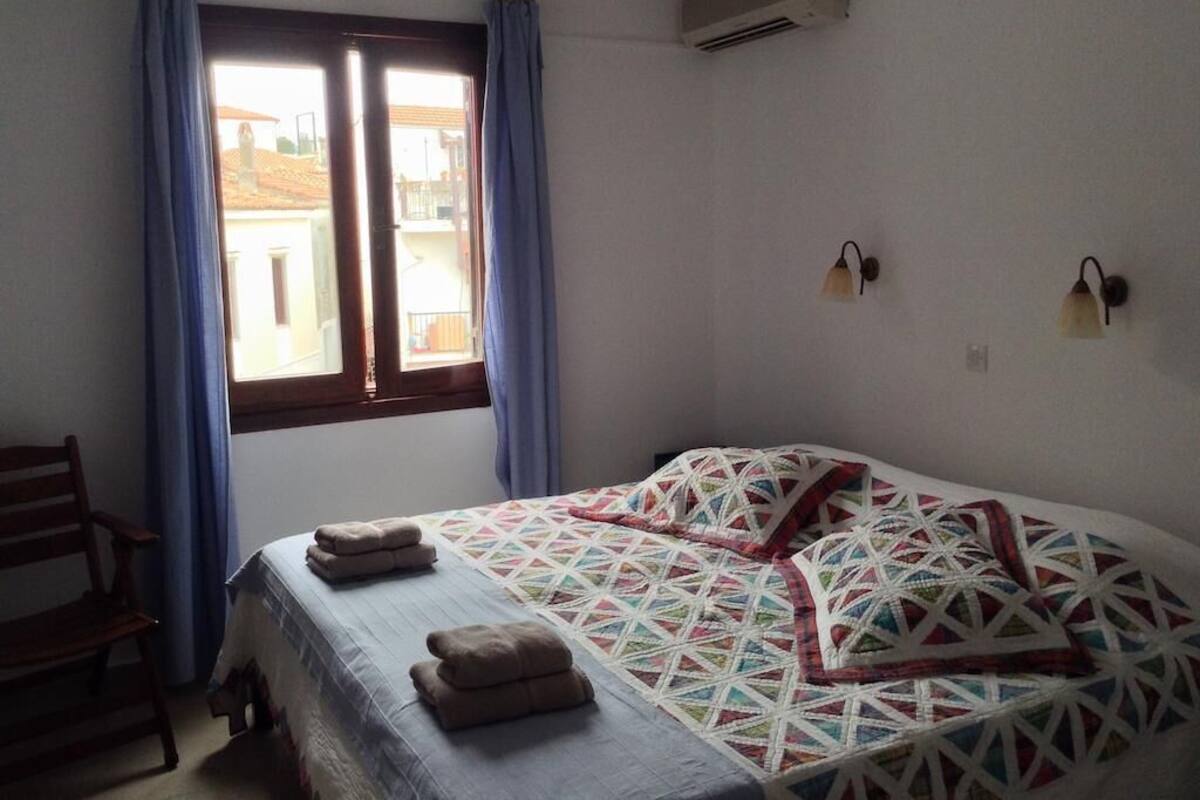 Un dormitorio con cama, una silla, una ventana con cortinas y un aire acondicionado de pared.